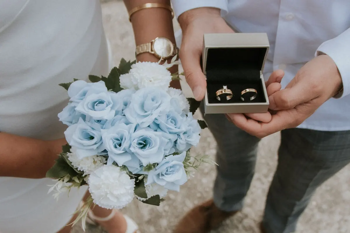 Un ramo de rosas azules y una caja con dos alianzas, en las manos de una pareja
