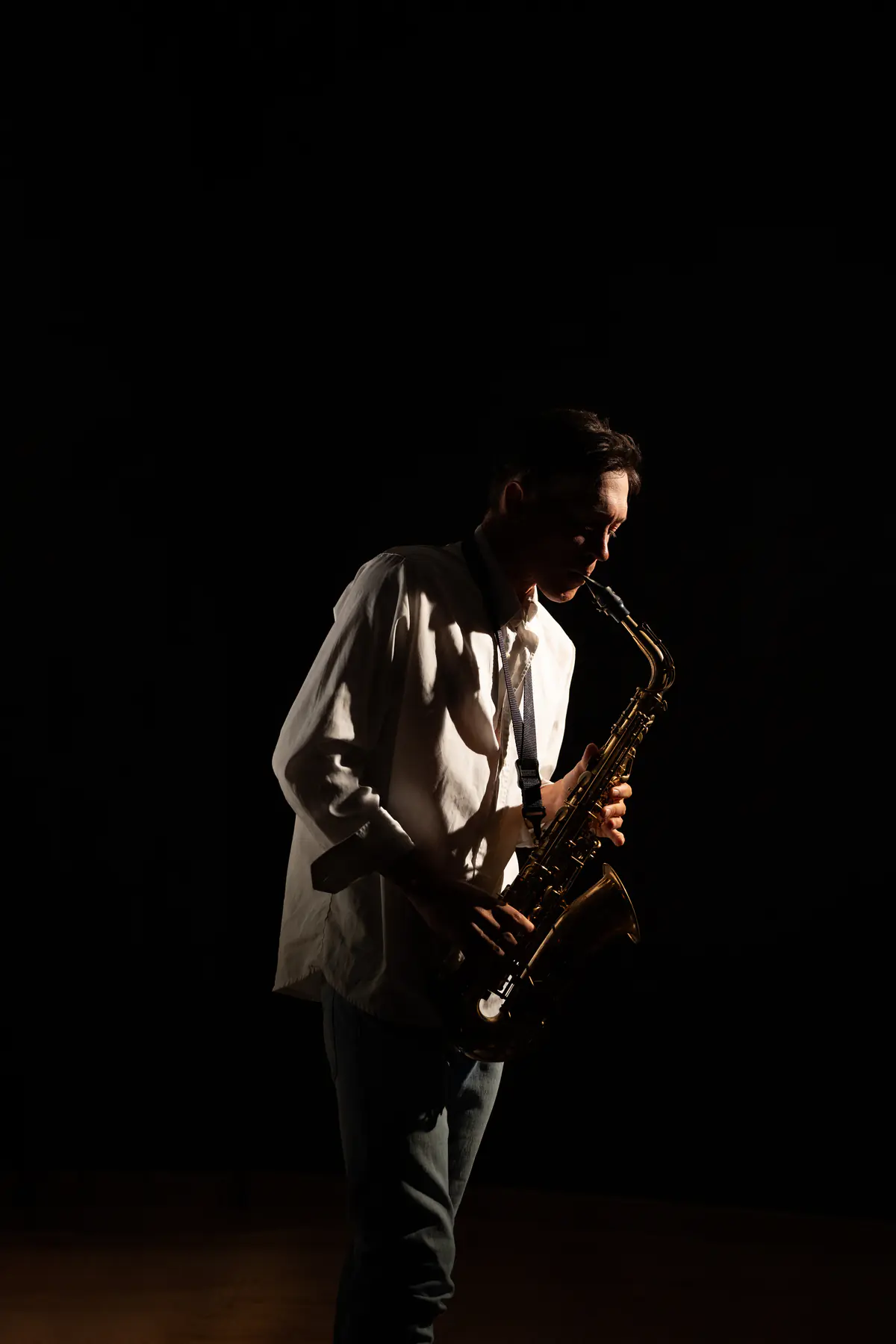 Zirano tocando el saxofón en penumbra con camisa blanca