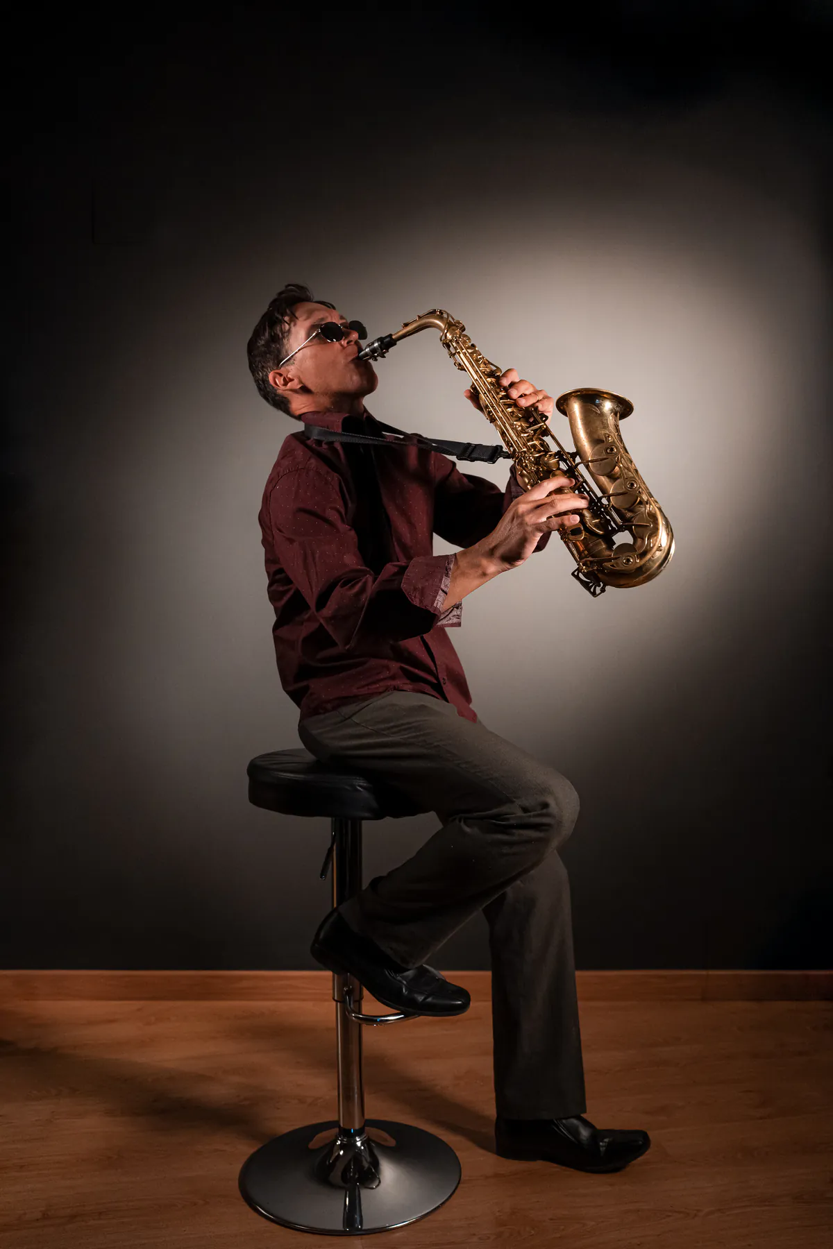 Zirano con gafas de sol tocando el saxofón bajo un foco