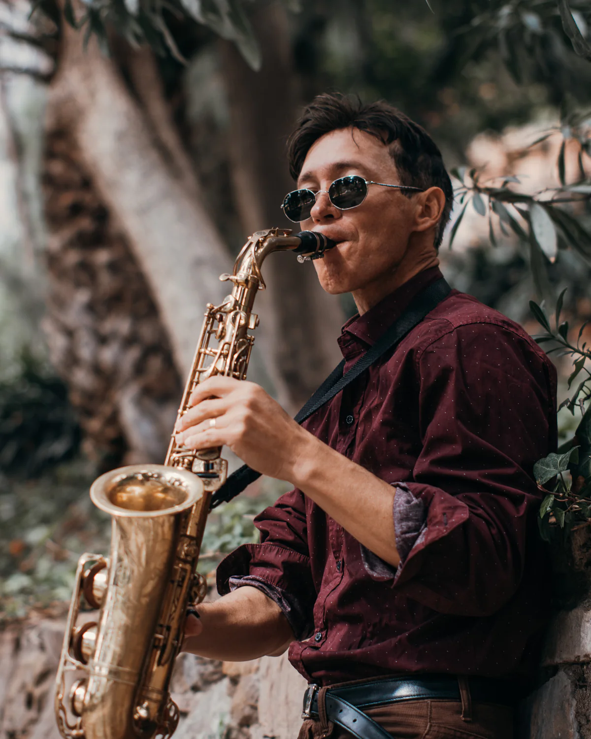 Zirano con gafas de sol tocando el saxofón junto a un muro de piedra
