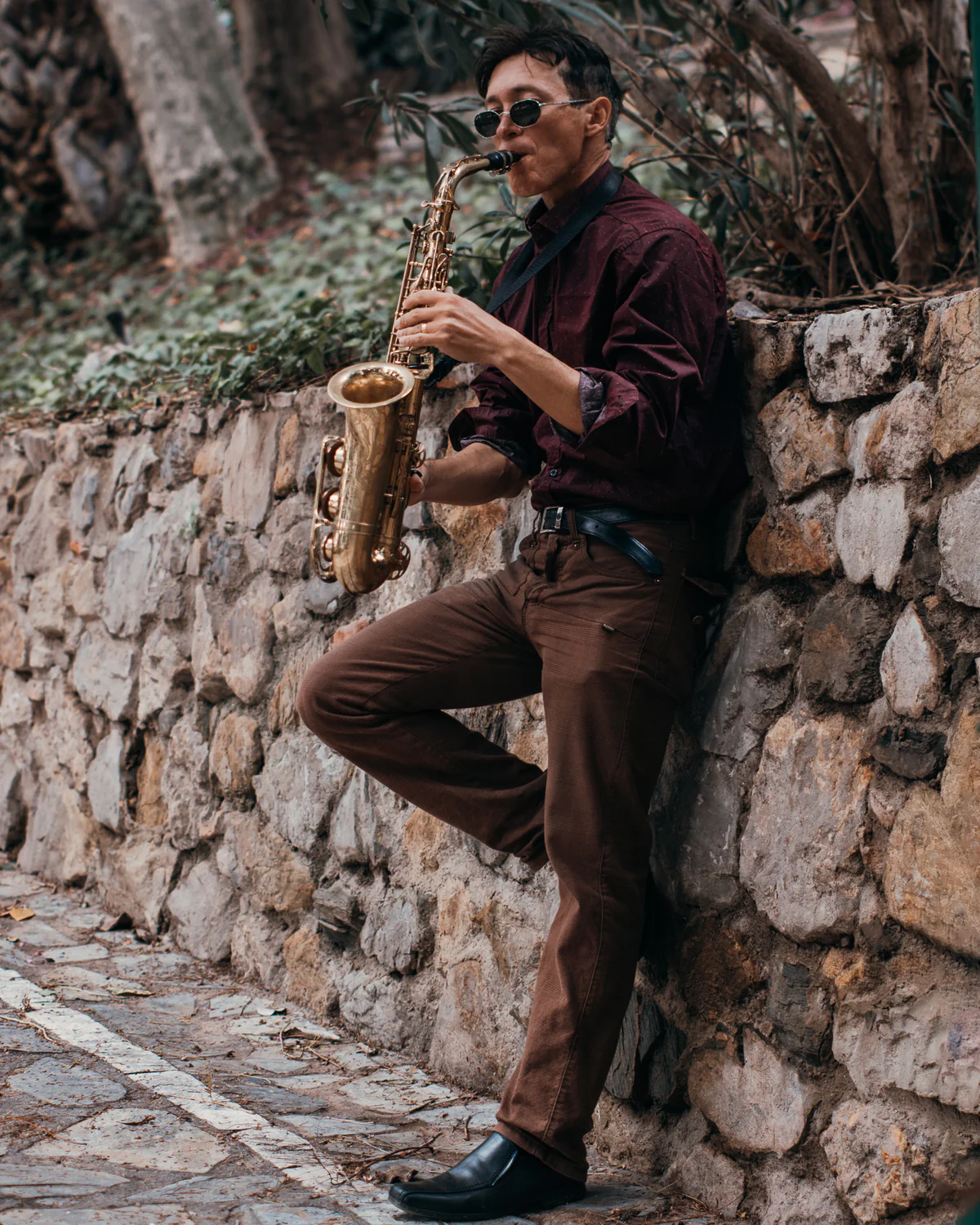 Zirano apoyado en un muro de piedra tocando el saxofón