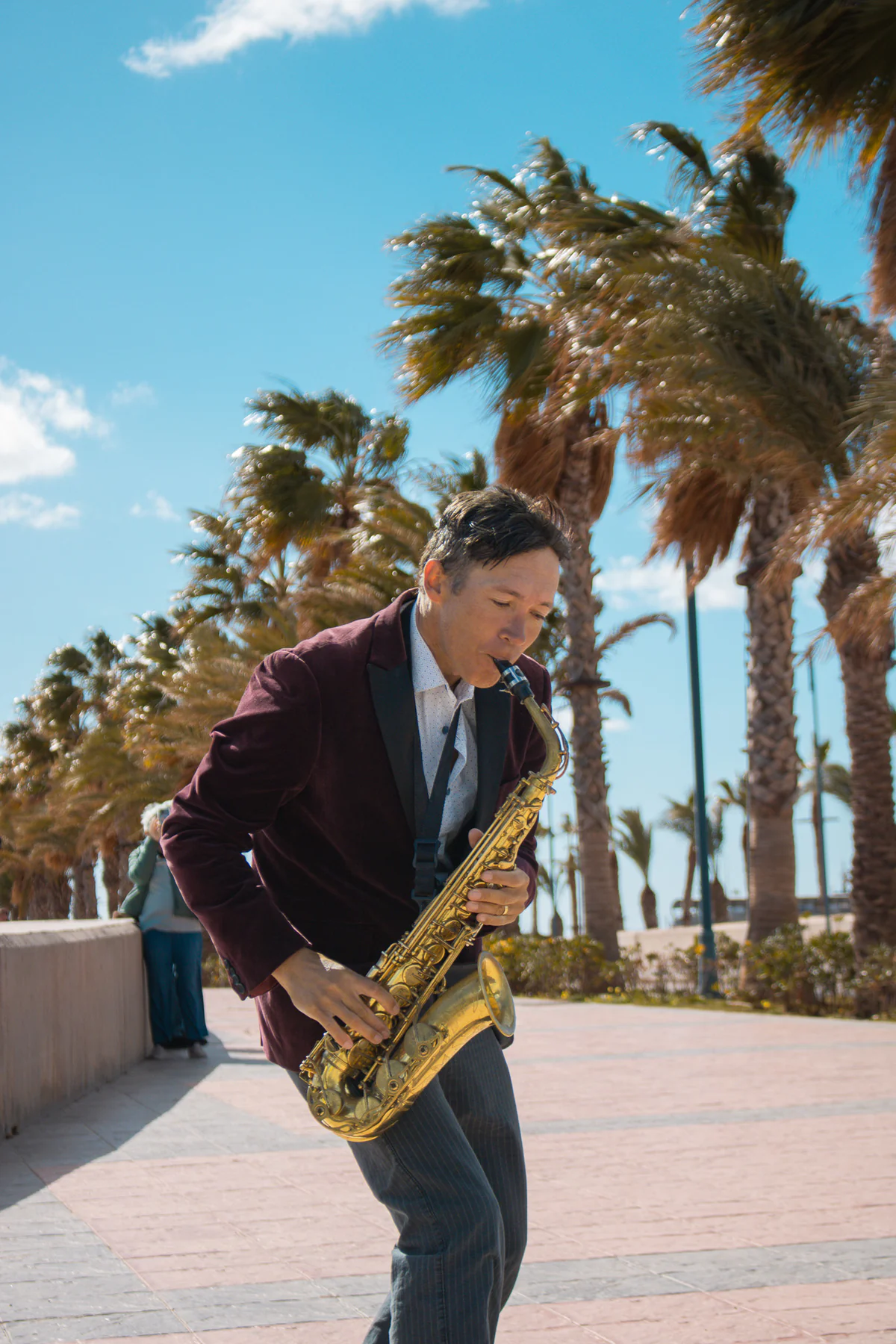 Zirano tocando el saxofón en el paseo marítimo entre palmeras