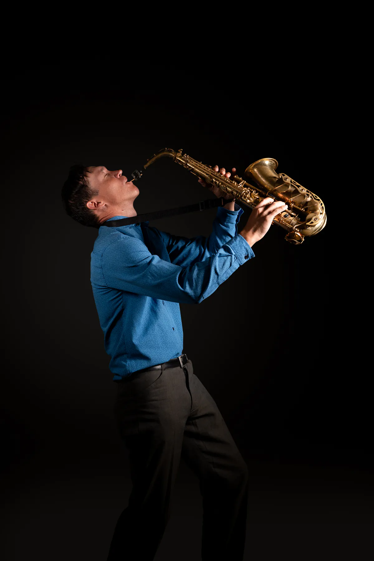 Zirano tocando el saxofón hacia arriba, con camisa azul y fondo negro