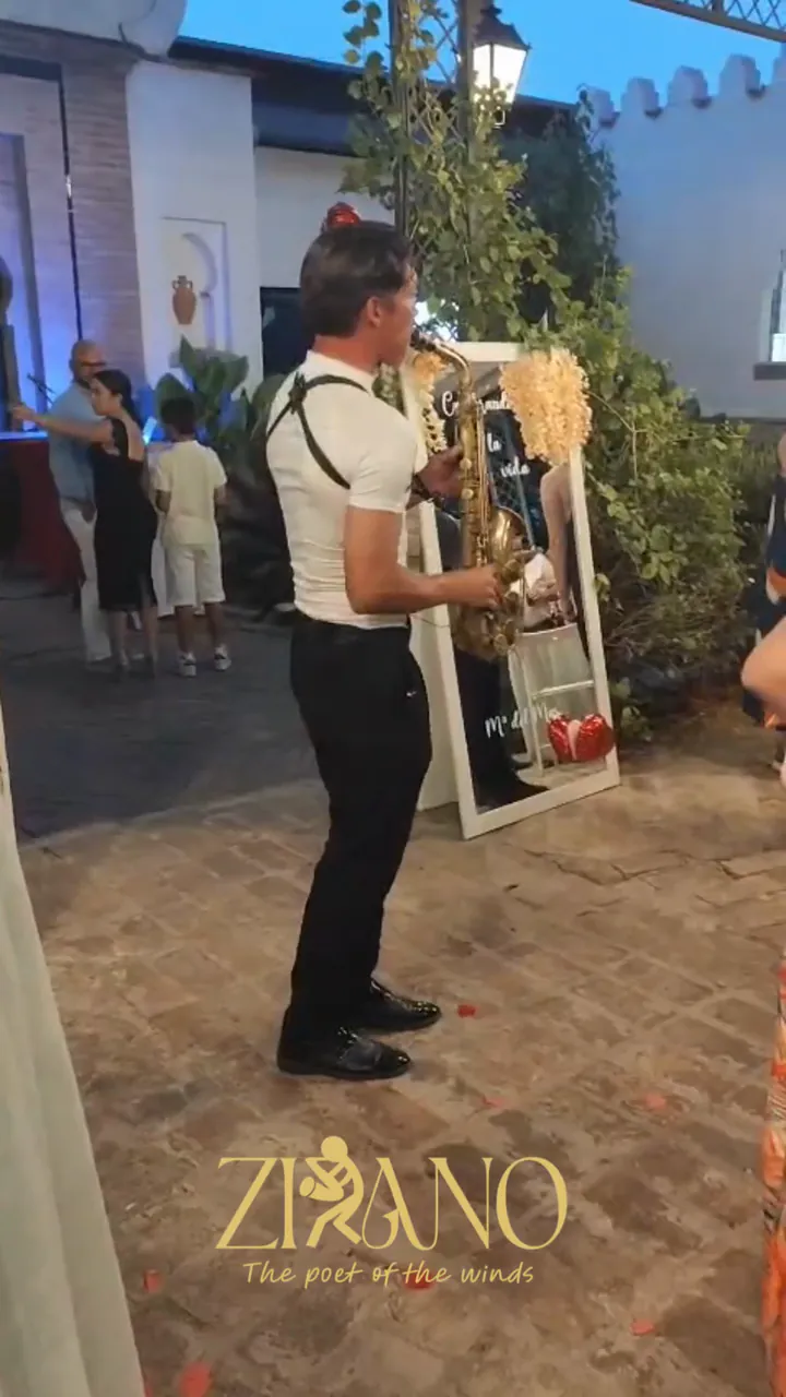 Zirano tocando el saxofón entre los invitados de un evento al aire libre, de noche