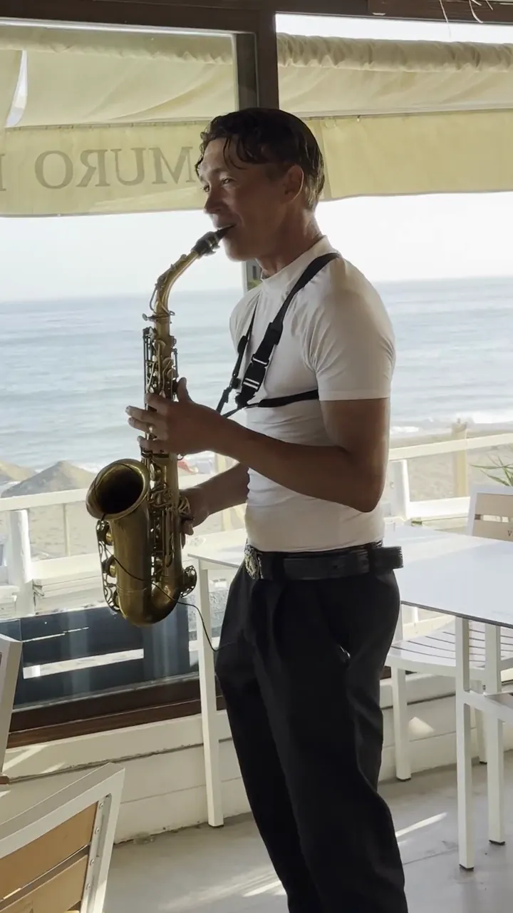 Zirano tocando el saxofón en un restaurante, con el mar detrás